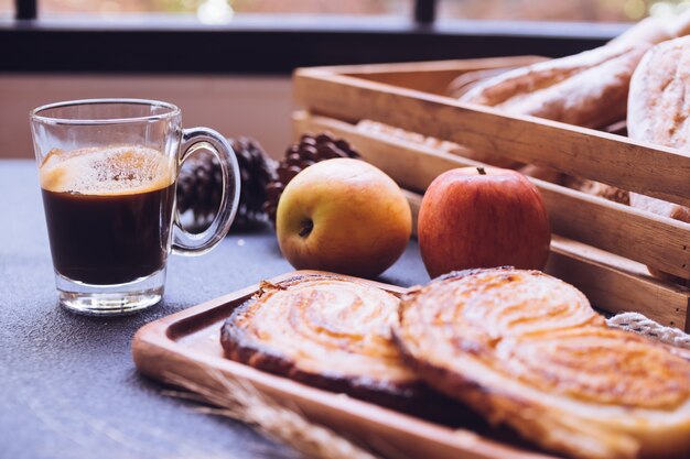 Gros plan de pains cuits au four, des pommes et une tasse de café sur une table.