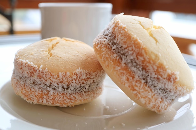 Gros plan une paire de biscuits Alfajores sur plaque blanche avec tasse blanche floue en arrière-plan