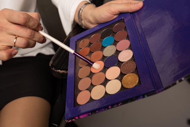 Gros plan sur une palette d'ombres multicolores entre les mains d'une maquilleuse. Outils de maquillage