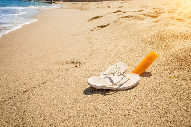 Gros plan sur des pantoufles blanches et une crème solaire au bord de la mer