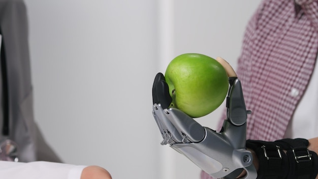 Gros plan sur un patient tenant une pomme dans un bras bionique lors d'une visite chez un médecin dans une clinique moderne