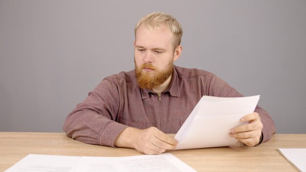 Gros plan d'un patron masculin gai avec barbe assis à une table avec des documents au bureau beau ...