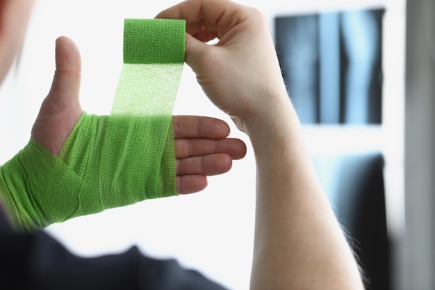 Gros plan sur une personne de sexe masculin bandant la main avec un bandage médical vert pour augmenter la circulation sanguine et