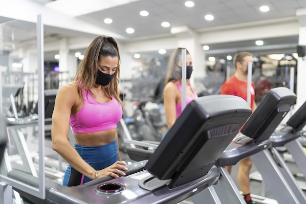 Gros plan de personnes faisant de l'exercice dans la salle de sport avec des masques faciaux - concept de nouvelle normalité