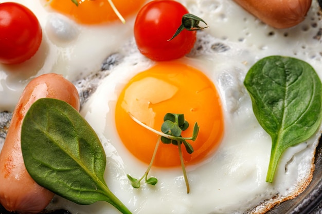 Gros plan d'un petit-déjeuner aux œufs frits avec des saucisses aux épinards et tomates cerises aux œufs