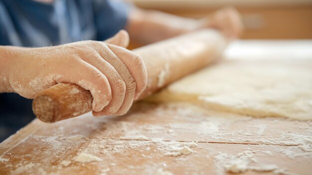 Gros plan d'un petit enfant utilisant un rouleau à pâtisserie en bois pour préparer la pâte à pizza