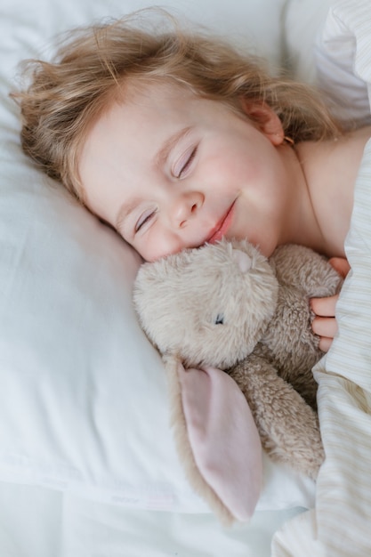 Gros plan d'une petite fille endormie et étreignant son lapin en peluche. Relaxation. Un sommeil sain. Confortable.