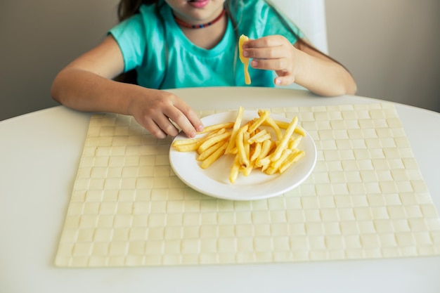 Gros plan d'une petite fille mangeant des frites à la cuisine
