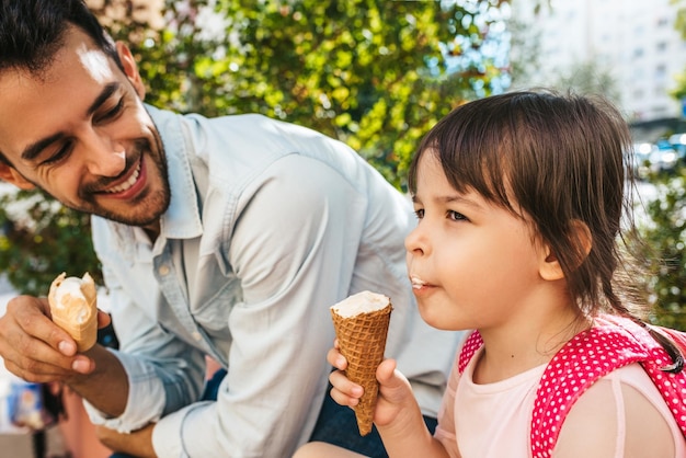 Gros plan d'une petite fille mignonne et heureuse assise avec un beau papa dans la rue de la ville et mangeant des glaces en plein air Une fille amusante et son père s'amusent à l'extérieur Bonne relation entre papa et fille