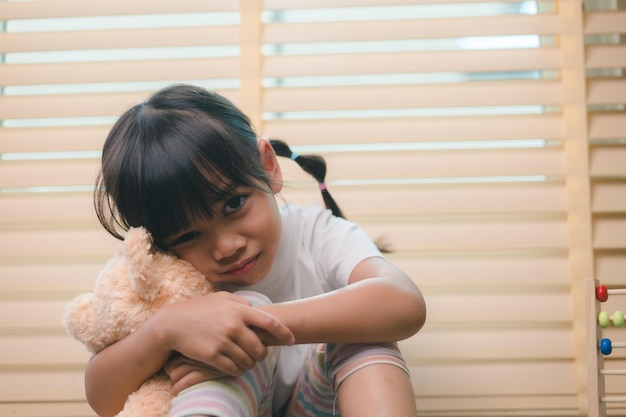 Gros plan sur une petite fille solitaire étreignant un jouet assis seul à la maison contrarié un enfant malheureux attendant que les parents réfléchissent aux problèmes de mauvaise relation dans un traumatisme psychologique familial