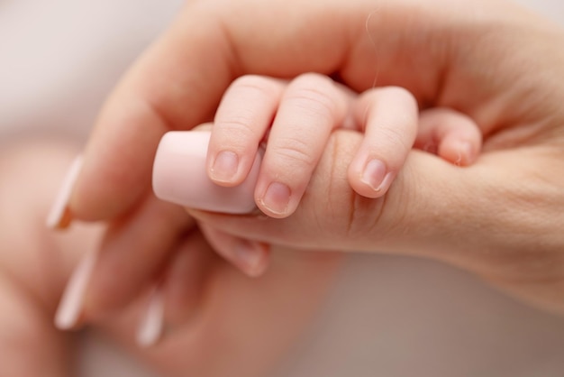 Gros plan d'une petite main de bébé avec de petits doigts et le bras de la mère sur un fond blanc Nouveau-né tenant le doigt des parents après la naissance Le lien entre la mère et l'enfant Concept de famille heureuse