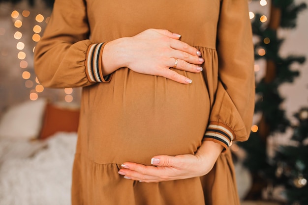 Gros plan photo du ventre de la mère enceinte dans des vêtements beiges Mains sur le ventre En attendant la naissance d'un enfant Maternité et grossesse