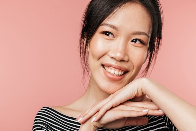 Gros plan photo d'une femme asiatique joyeuse vêtue de vêtements de base souriante et regardant de côté isolée sur un mur rouge