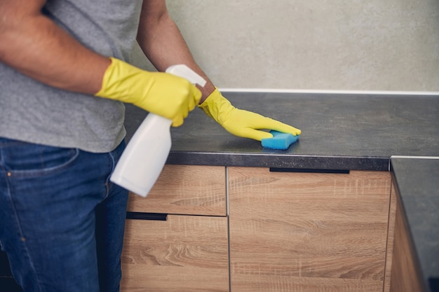 Gros plan photo de l'homme cin gants jaunes avec détergent et caoutchouc dans la cuisine