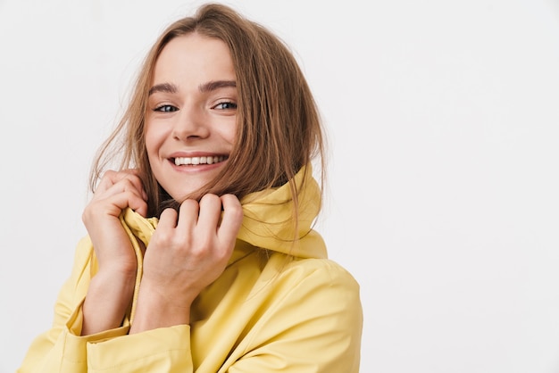 Gros plan photo de joyeuse jeune femme en imperméable regardant la caméra et souriant