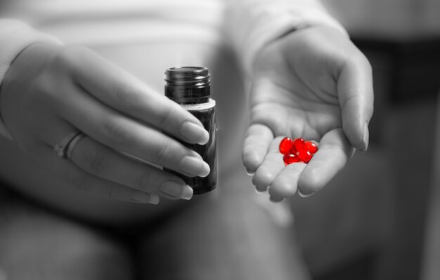 Gros plan photo en noir et blanc d'une femme enceinte tenant une pilule rouge à portée de main