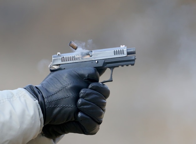 Gros plan Photo d'un pistolet tirant à deux mains, les obus émanant du volet et de la fumée bleue.