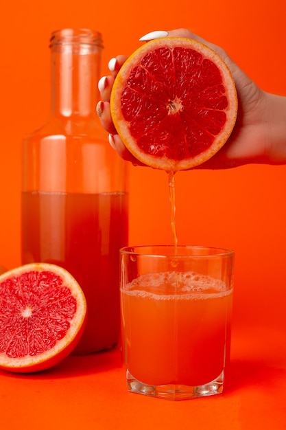 Gros plan photo recadrée d'une femme tenant dans les mains la moitié d'une tasse en verre de pamplemousse mûr frais