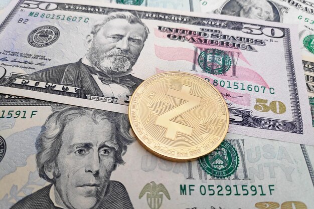 Gros plan sur une pièce de monnaie Zcash dorée au-dessus d'une pile de billets en dollars américains