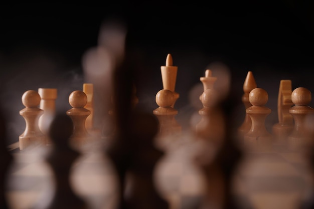 Gros plan de pièces d'échecs blanches à bord avec dissipation de la vapeur Deux rangées de figures en bois sur l'échiquier sur fond noir Concept de jeu logique et stratégique intelligent