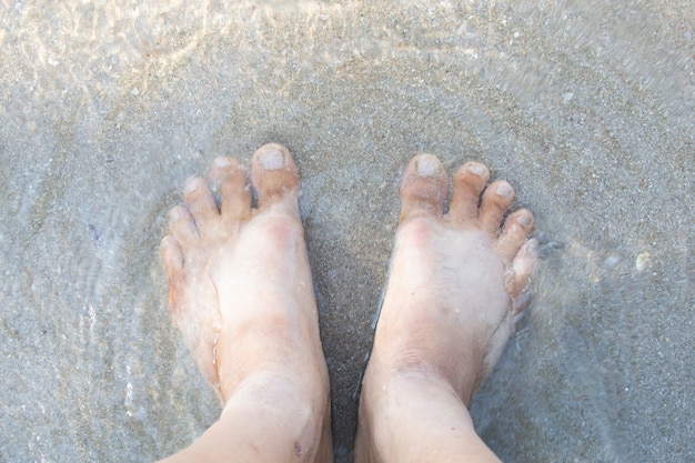 Gros plan des pieds dans l&#39;eau de mer sur la plage.