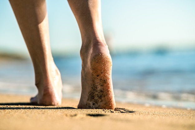 Gros plan des pieds de femme marchant pieds nus sur le sable, laissant des empreintes sur la plage dorée. Concept de vacances, voyages et liberté. Les gens se détendent en été.