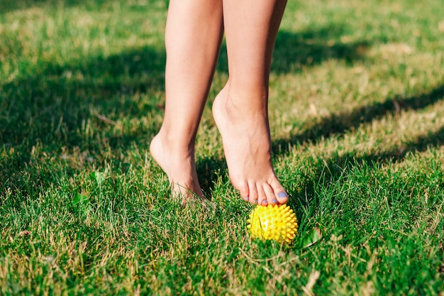 Gros plan sur les pieds nus gracieux d'une jeune femme debout sur la pointe des pieds sur une boule de massage à pointes sur la pelouse verte de la cour d'été, concept de physiothérapie.