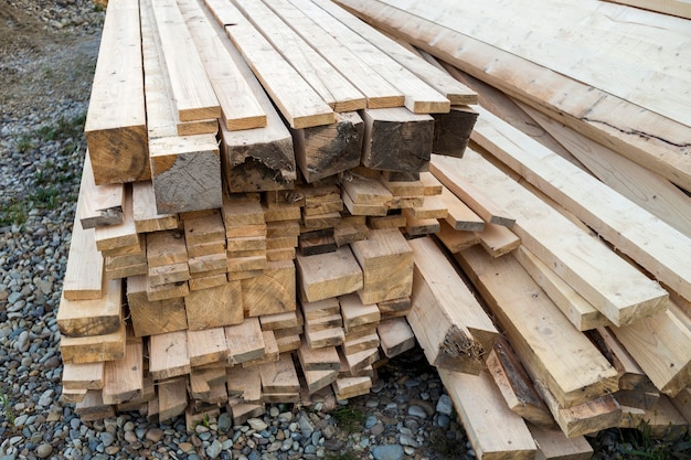 Gros plan sur une pile empilée de planches de bois brut inégales brunes naturelles éclairées par un soleil éclatant. Bois industriel pour la menuiserie, la construction, la réparation et l'ameublement, bois de charpente pour la construction.