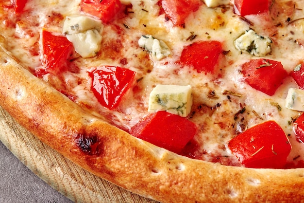 Gros plan de pizza aux tomates mozzarella, fromage bleu et basilic séché sur planche de bois