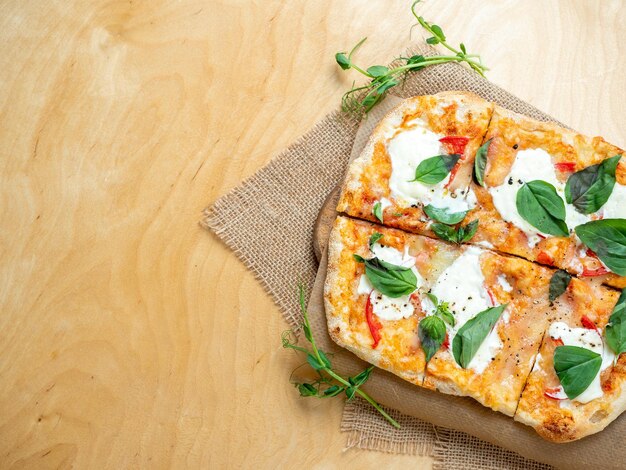 Gros plan d'une pizza romaine fraîche et chaude avec des tomates et du fromage strachatella sur un fond en bois brut Cuisine italienne verts à proximité Vue de dessus espace de copie plat