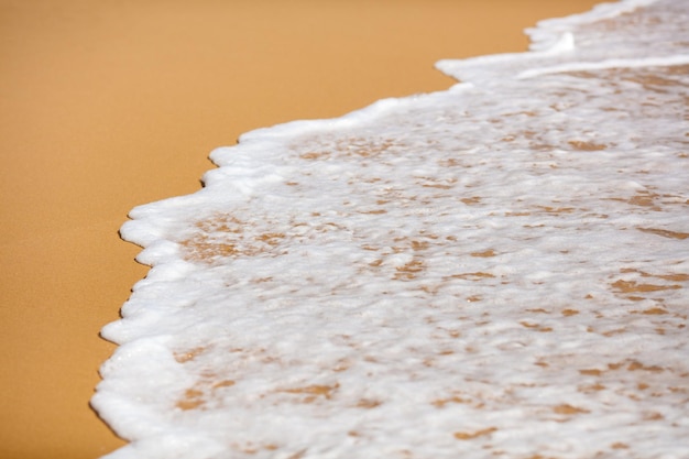 Gros plan sur une plage de sable tropicale avec des vagues de mer mousseuses