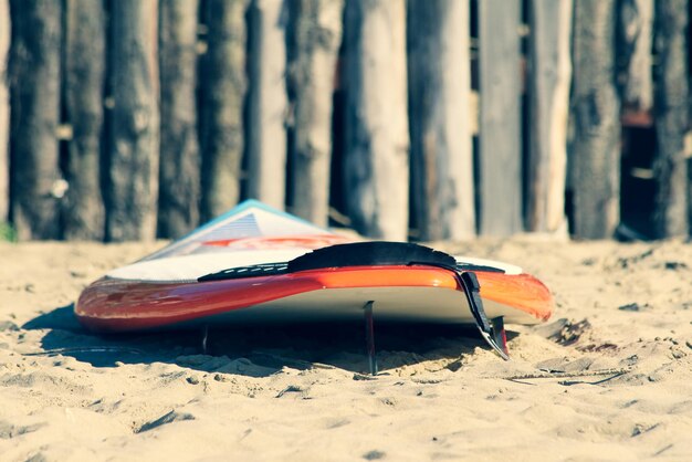 Gros plan d'une planche de surf à la mode au lever ou au coucher du soleil sur la plage de sable Clôture en bois sur le fond Concept de vacances Vacances d'été Tourisme sport Espace de copie horizontal pour le texte