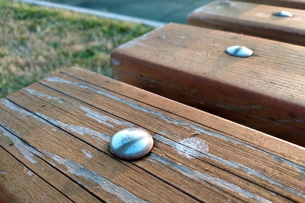 Gros plan des planches de bois fixées avec des clous métalliques sur un banc à l'extérieur.