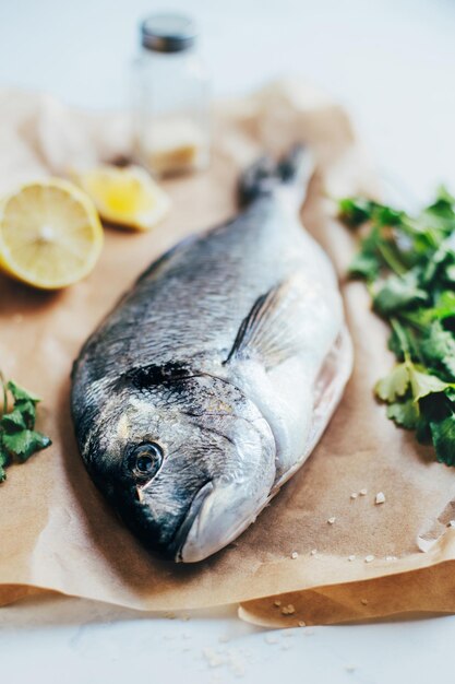 gros plan de poisson dorado cru sur parchemin sur fond de persil et de citron tranché sur fond blanc