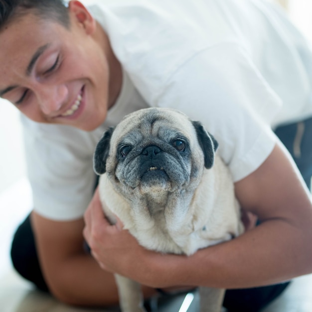 Gros plan et portrait de deux meilleurs amis à la maison ensemble - adolescent regardant avec amour son carlin - concept de chien de compagnie et de chien domestique