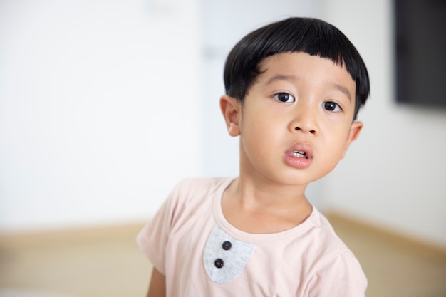 Gros plan portrait enfant asiatique garçon cheveux noirs tout droit portant une chemise marron clair regardant la caméra