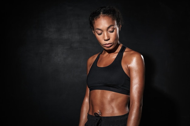 Gros plan portrait d'une femme afro-américaine sérieuse en tenue de sport debout isolée sur fond noir