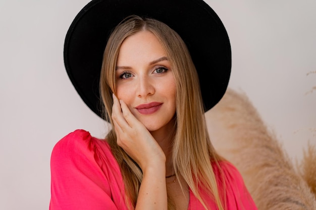 Gros plan portrait femme blonde au chapeau noir et robe d'encre posant en studio en studio avec décor d'herbe de la pampa