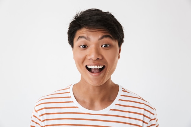 Gros plan Portrait d'un homme chinois excité et heureux portant un t-shirt rayé souriant avec des dents parfaites et en vous regardant, isolé. Concept d'émotions