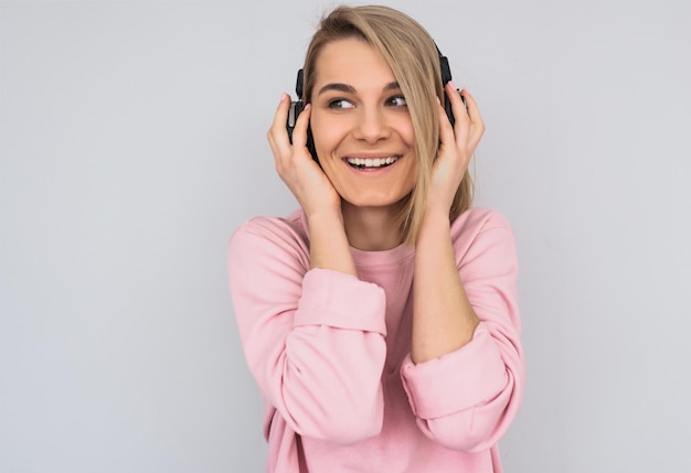 Gros plan portrait horizontal en studio d'une jeune femme souriante heureuse portant un pull rose regardant de côté tenant un casque avec les mains écoutant de la musique préférée isolée sur fond blanc Espace de copie