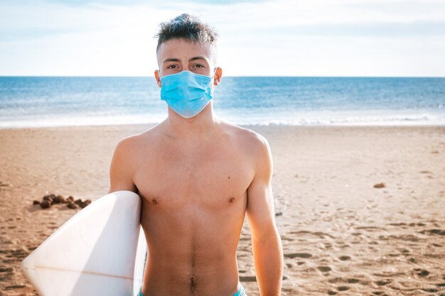 Gros plan et portrait d'un jeune homme ou d'un adolescent regardant la caméra portant sérieusement un masque pour prévenir les maladies et le virus du surf pour la contamination de la mer et l'écologie de la nature