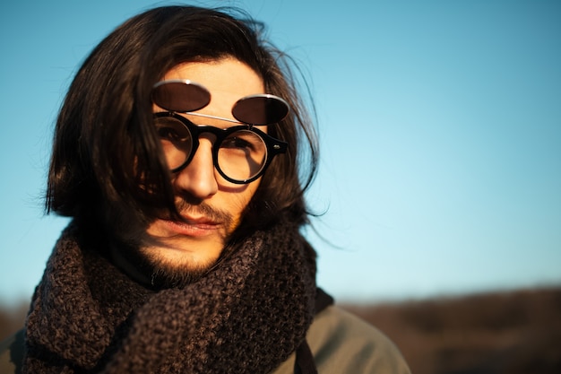 Gros plan portrait de jeune homme aux cheveux longs portant des lunettes de soleil rondes hipster et une écharpe.
