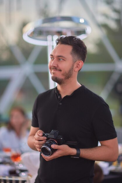 Gros plan portrait d'un jeune homme élégant avec une barbe et des cheveux noirs dans un T-shirt noir Le photographe masculin utilise un appareil photo sans miroir pour prendre une photo