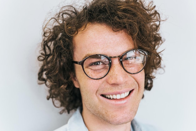 Gros plan portrait recadré d'un beau mâle positif aux taches de rousseur avec un sourire à pleines dents sain posant pour la publicité isolé sur un mur blanc avec un espace de copie pour votre information ou votre contenu