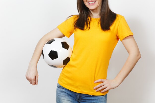 Gros plan portrait recadré Jeune femme européenne, fan de football ou joueur en uniforme jaune tenant un ballon de football isolé sur fond blanc. Sport, jouer au football, santé, concept de mode de vie sain.