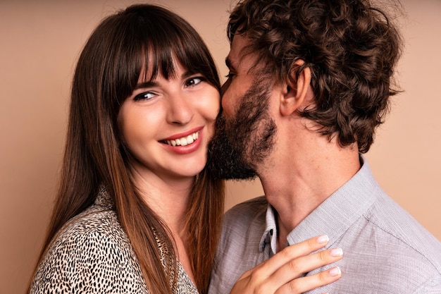 Gros plan portrait en studio d'un couple amoureux d'âge moyen, câlins et bisous, heureux ensemble, tenues de soirée glamour, prêt pour la célébration, fond beige.