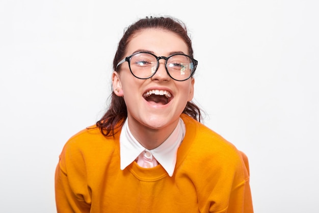 Gros plan portrait en studio d'une jeune femme heureuse souriante porte largement un pull orange et des lunettes rondes transparentes Jolie fille étudiante posant sur un mur de studio blanc Personnes et émotions