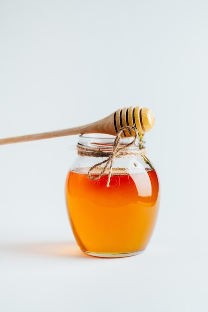 Gros plan sur un pot de miel et une broche en bois pour le miel sur fond blanc