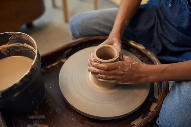 Gros plan d'un potier méconnaissable assis au tour de potier et créant un pot en céramique en atelier