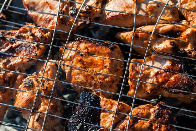 Photo gros plan sur le processus de cuisson du shashlik de viande de porc ou de boeuf serré dans un gril avec une croûte brûlée croustillante sur des charbons gris brûlés sur un feu ouvert avec de la fumée qui monte